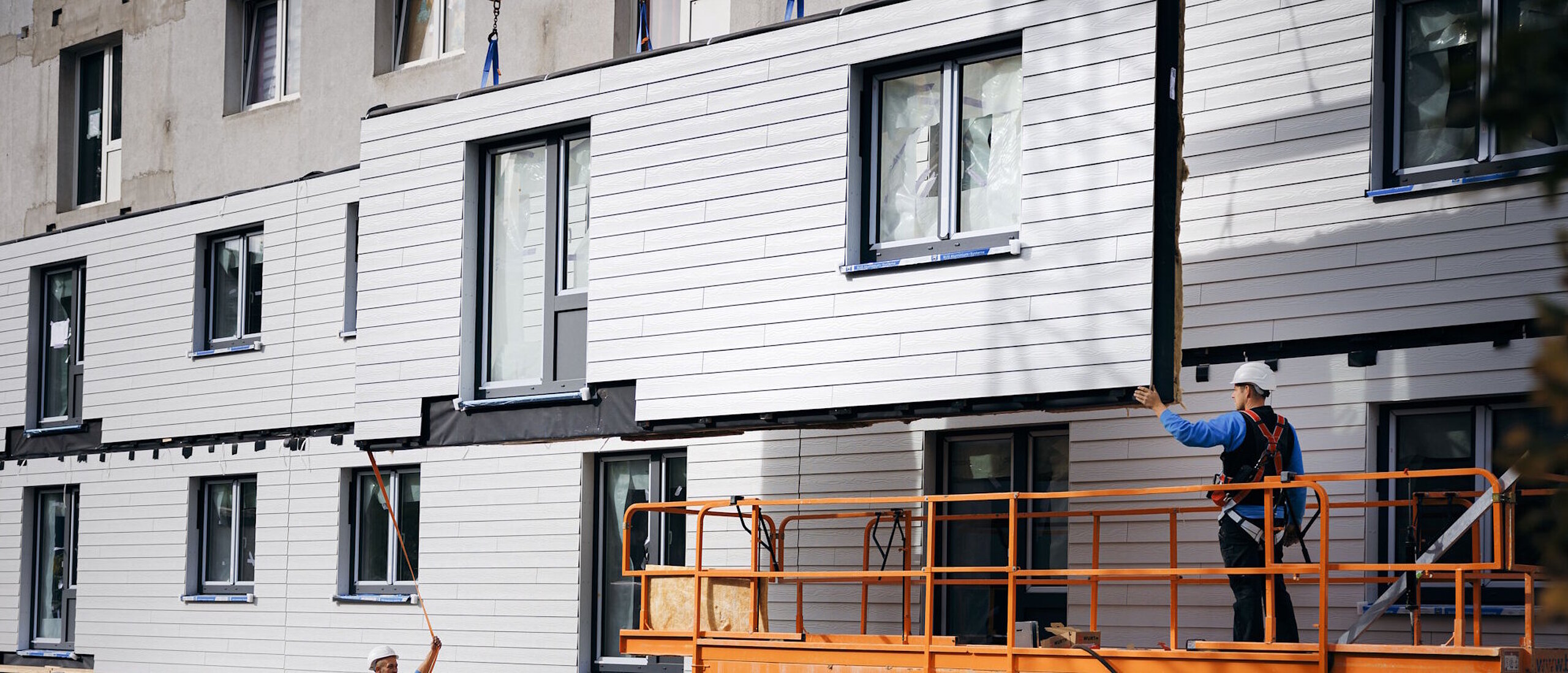 Mehrfamilienhaus während Sanierung, schwebendes, vorgefertigtes Fassadenlement, Bauarbeiter
