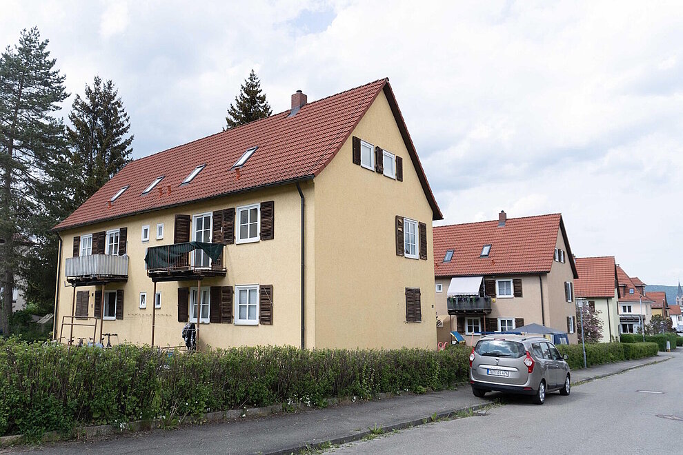 Mehrfamilienhaus mit Schrägdach vor Sanierung, davor eine Straße