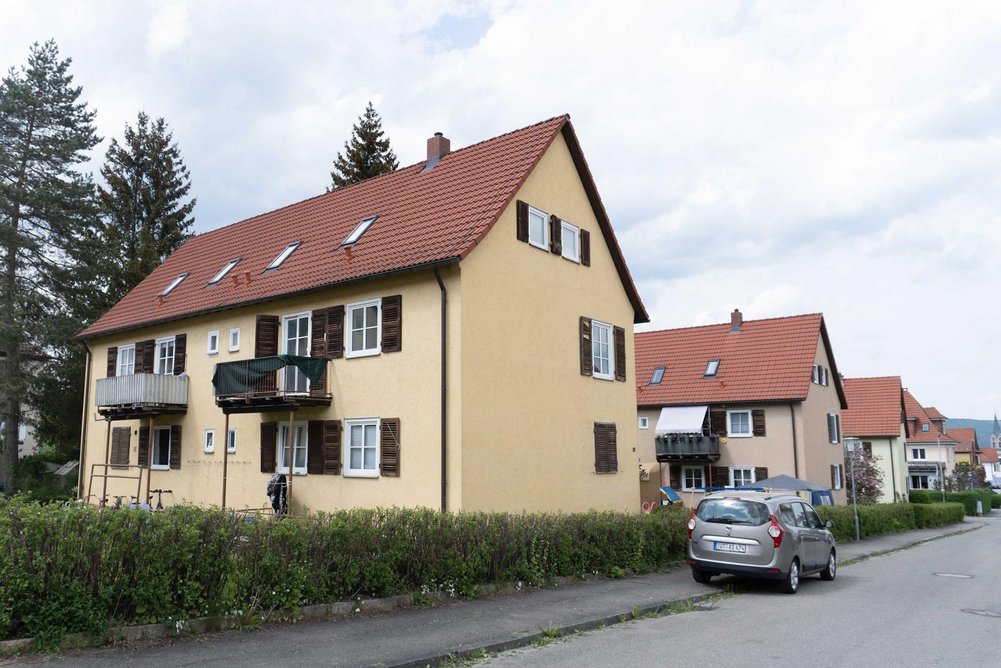 Mehrfamilienhaus mit Schrägdach vor Sanierung, davor eine Straße