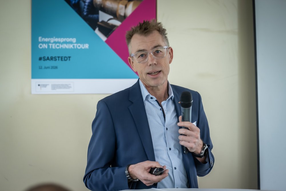 Gundolf Scholpp, Wolf GmbH Sprechende Person mit Mikrofon in der Hand, im Hintergrund Wand mit Poster