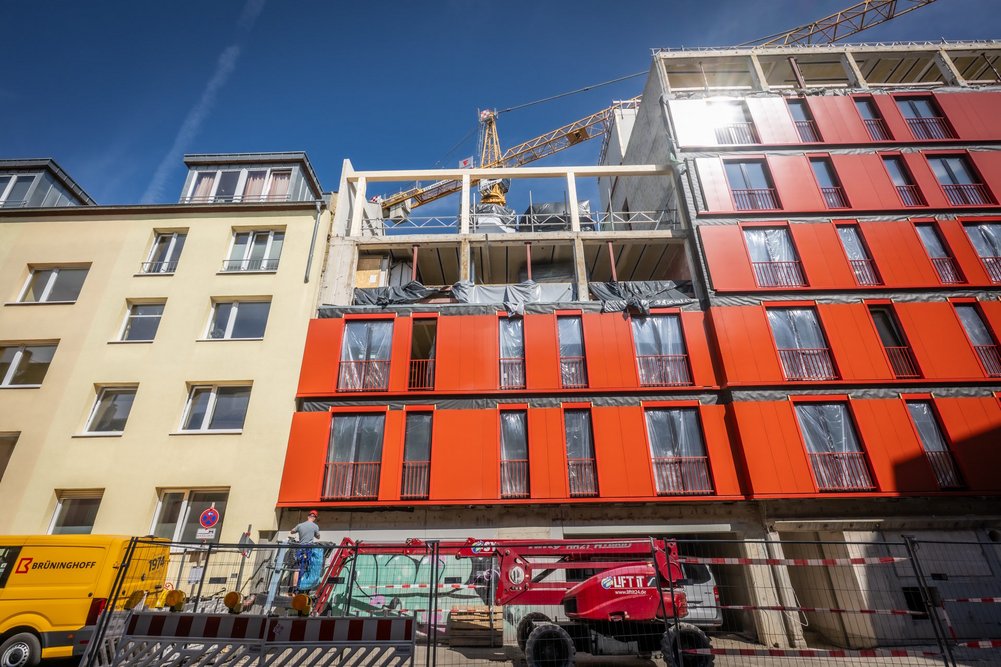 Umbau eines Verwaltungsgebäudes zu Studierendenapartments in Köln-Nippes Mehrstöckiges Gebäude während Sanierung mit roten vorgefertigten Fassadenelementen