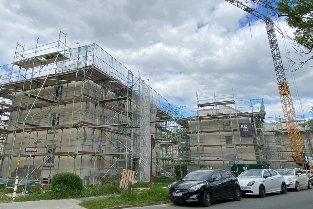 Mehrfamilienhäuser während Sanierung, davor ein Kran sowie eine Straße mit parkenden Autos