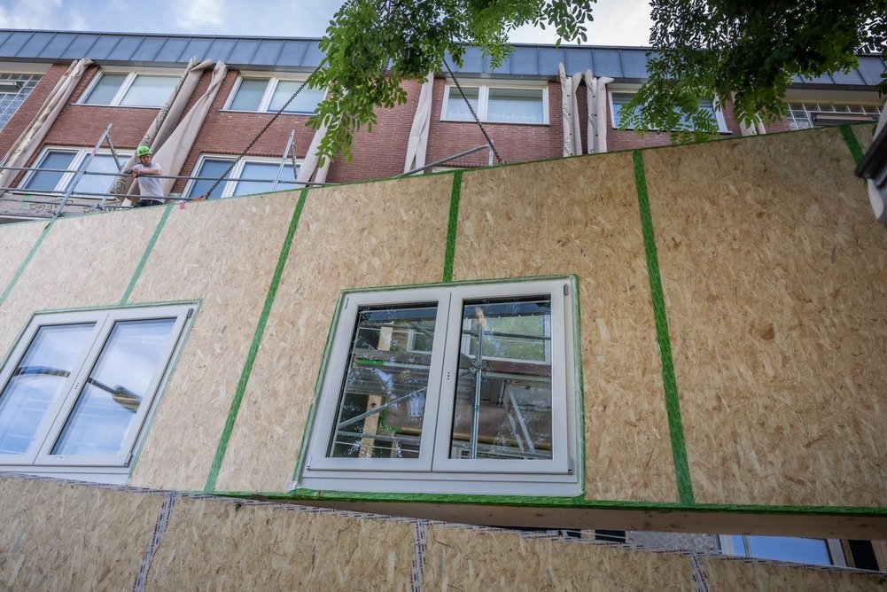Vorgefertigtes Fassadenelement mit Fenstern, im Hintergrund ein Mehrfamilienhaus