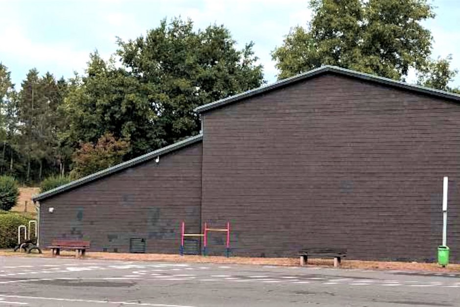 Außenansicht einer Turnhalle mit dunkler Holzfassade und Schrägdach