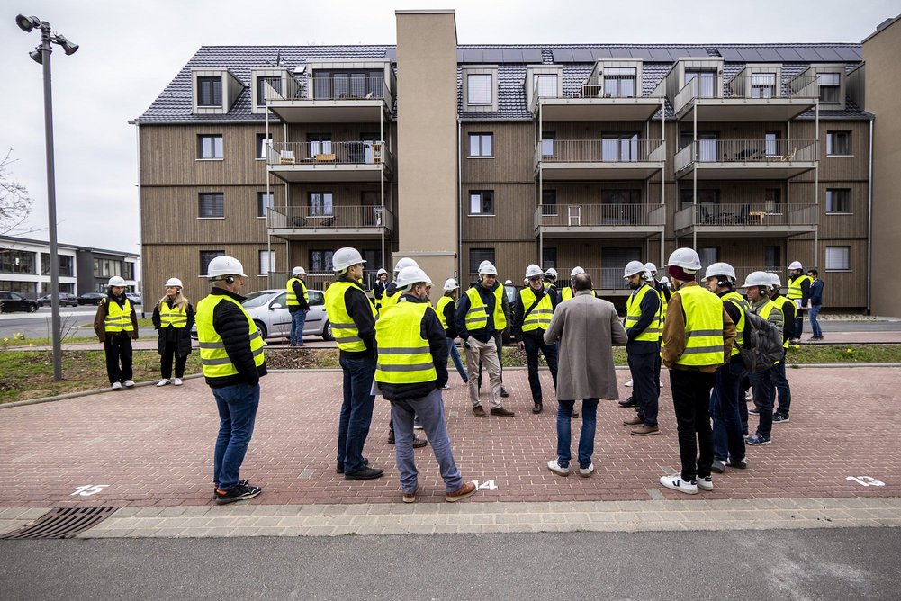 Energiesprong on tour Personen mit Sicherheitsweste und Bauhelm stehen vor Wohngebäude
