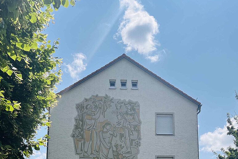 Frontansicht einer Mehrfamilienhauses, dreigeschossig mit Schrägdach, im Hintergrund blauer Himmel mit leichter Bewölkung