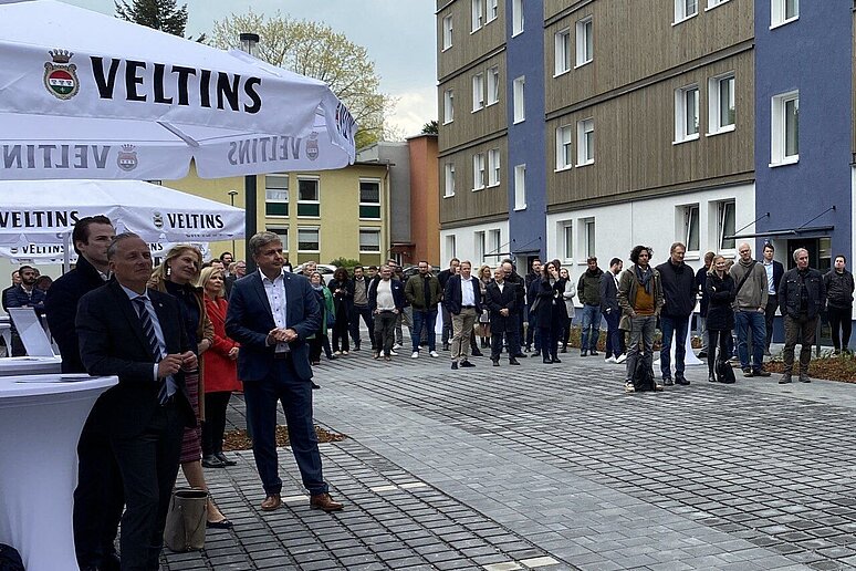 Menschenmenge mit Stehtischen vor Gebäude