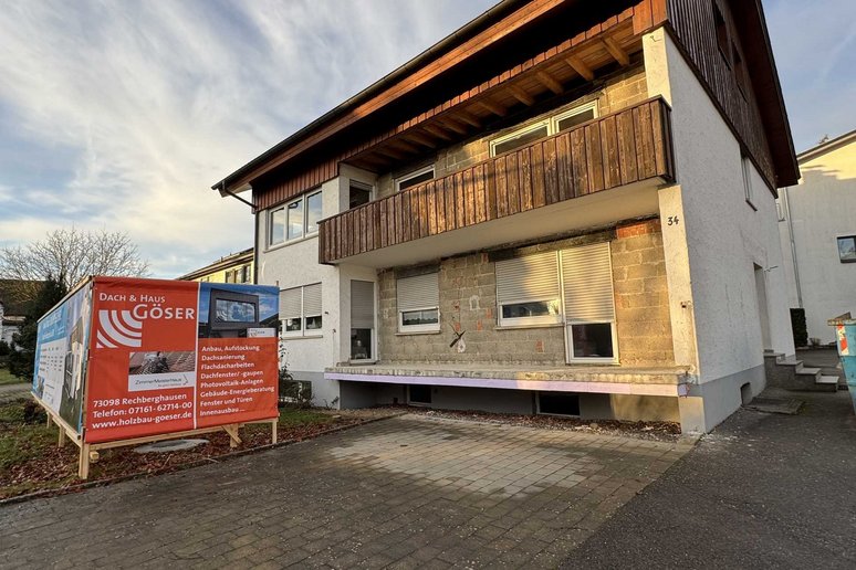 Bild zeigt: Zweifamilienhaus mit Holzverkleideten Balkonen und Bauschild davor