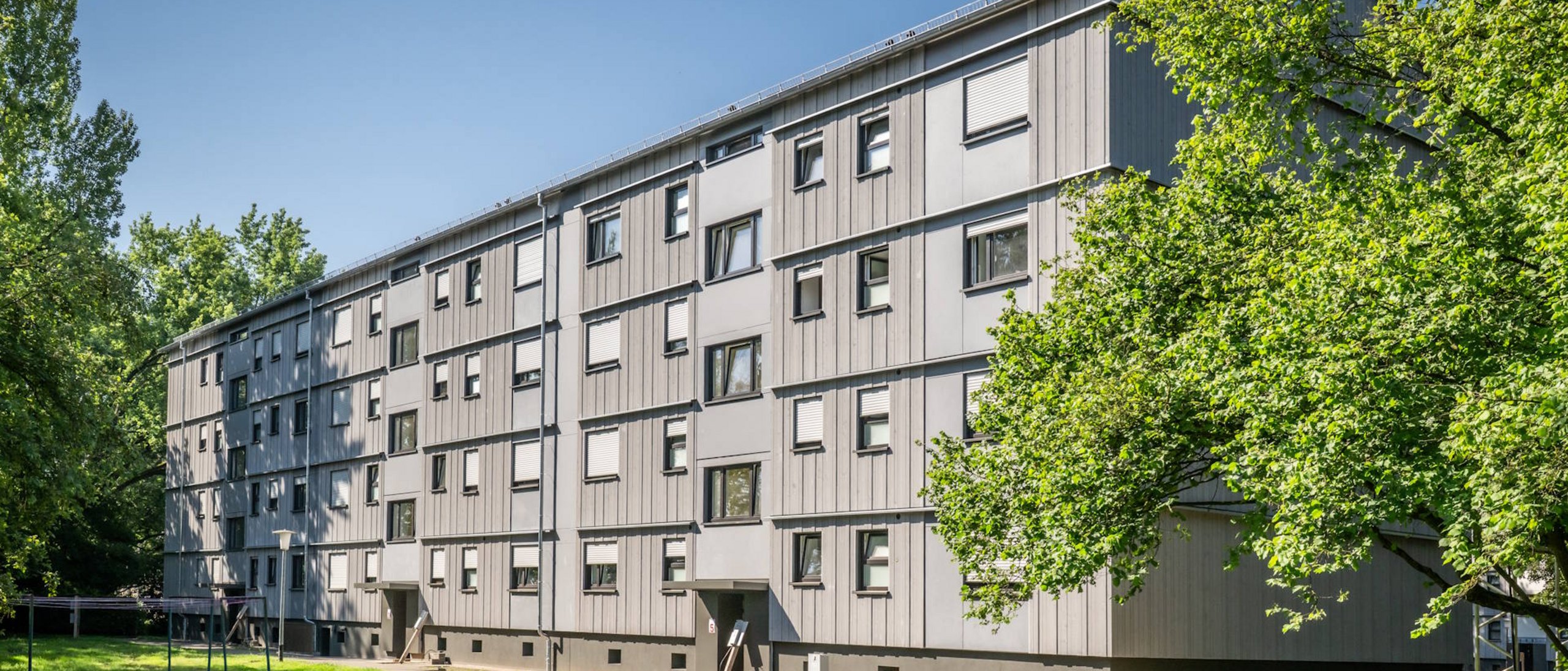Mehrfamilienhaus viergeschossig mit Schrägdach nach Sanierung, umgeben von Laubbäumen und Rasenfläche