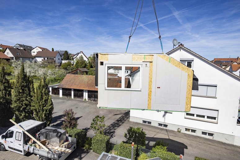Vorgefertigtes Hausfassadenelement schwebt vor einem Haus. 