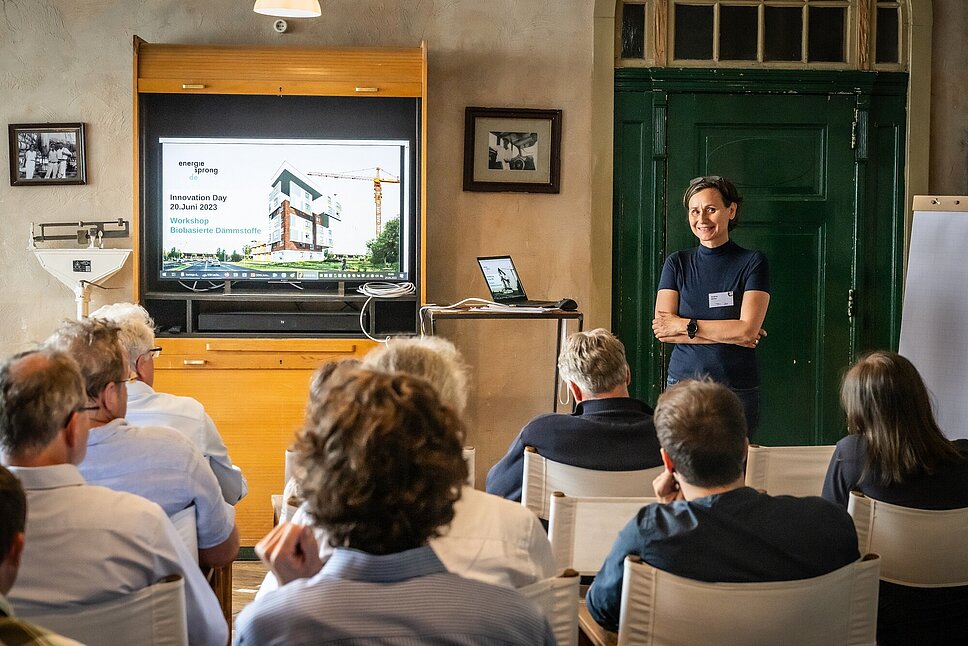 Workshop mit Teilnehmenden, die auf Stühlen sitzen und zur Referentin schauen.