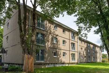 Mehrfamilienhaus dreigeschossig mit Schrägdach davor Rasenfläche und Laubbäume