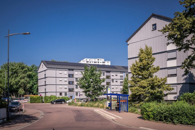 Straße durch ein Wohngebiet, auf der rechten Seite zwei neu sanierte Mehrfamilienhäuser viergeschossig und Grünanlagen