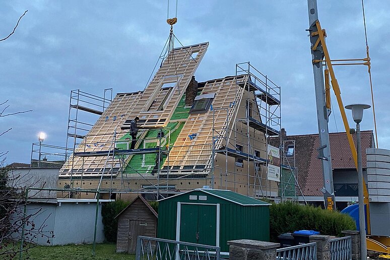 Baustelle in der Dämmerung mit Kran und schwebenden Dachelementen