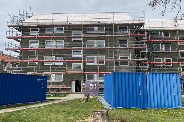 Mehrfamilienhaus viergeschossig mit Baugerüst während Sanierung, davor stehen zwei blaue Container.