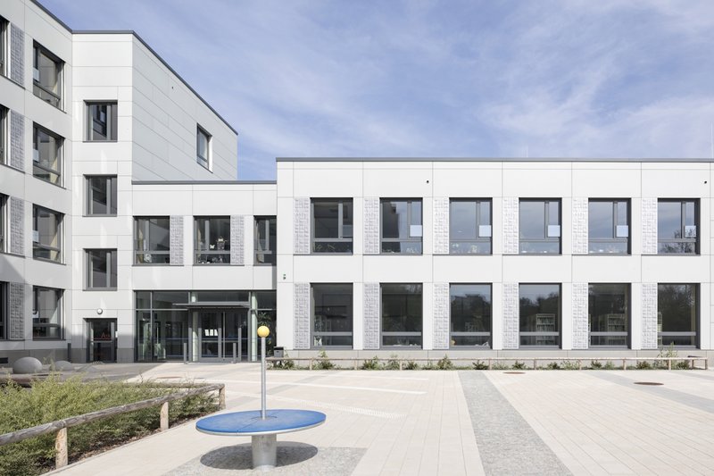 Schulgebäude nach Sanierung mit Pausenhof, helle Fassade mit großen Fenstern