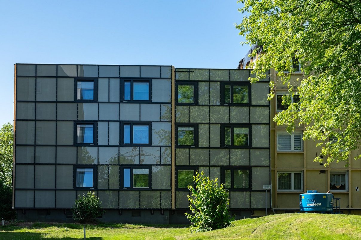 Frontansicht eines Mehrfamilienhause, davor Rasenfläche und ein Baum