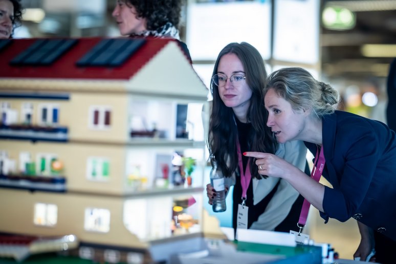 Zwei Frauen schauen sich interessiert ein Gebäudemodell aus Steckbausteinen an.