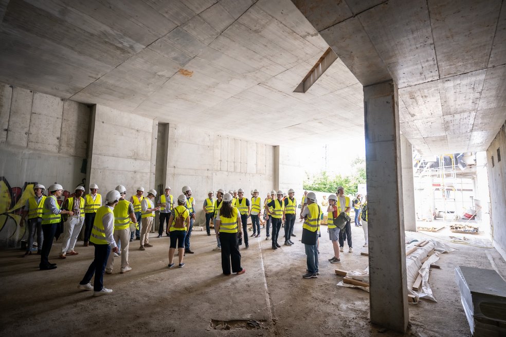 Personengruppe mit gelben Sicherheitswesten besichtigen Teil eines Gebäudes (Baustelle).
