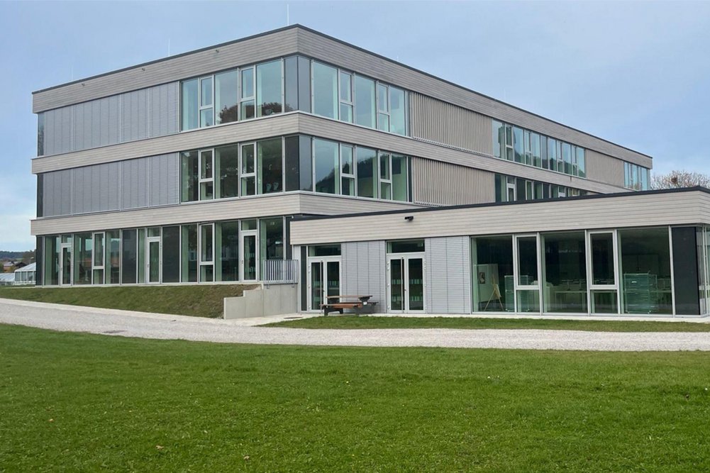 Modernes Schulgebäude dreigeschossig, davor Rasenfläche