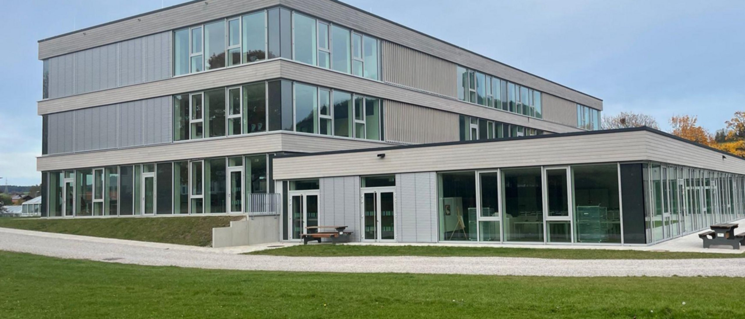 Modernes Schulgebäude dreigeschossig, davor Rasenfläche
