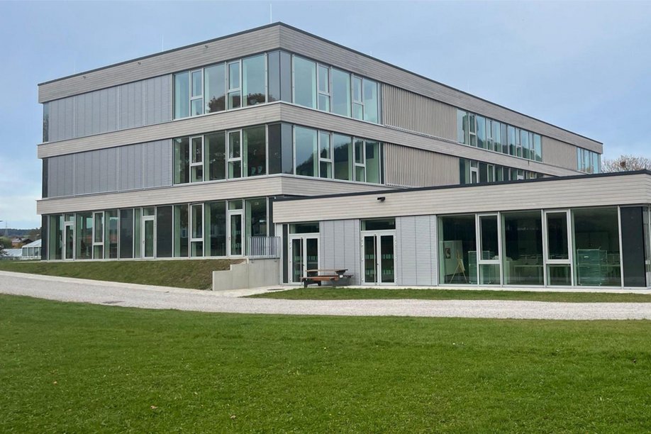Modernes Schulgebäude dreigeschossig, davor Rasenfläche