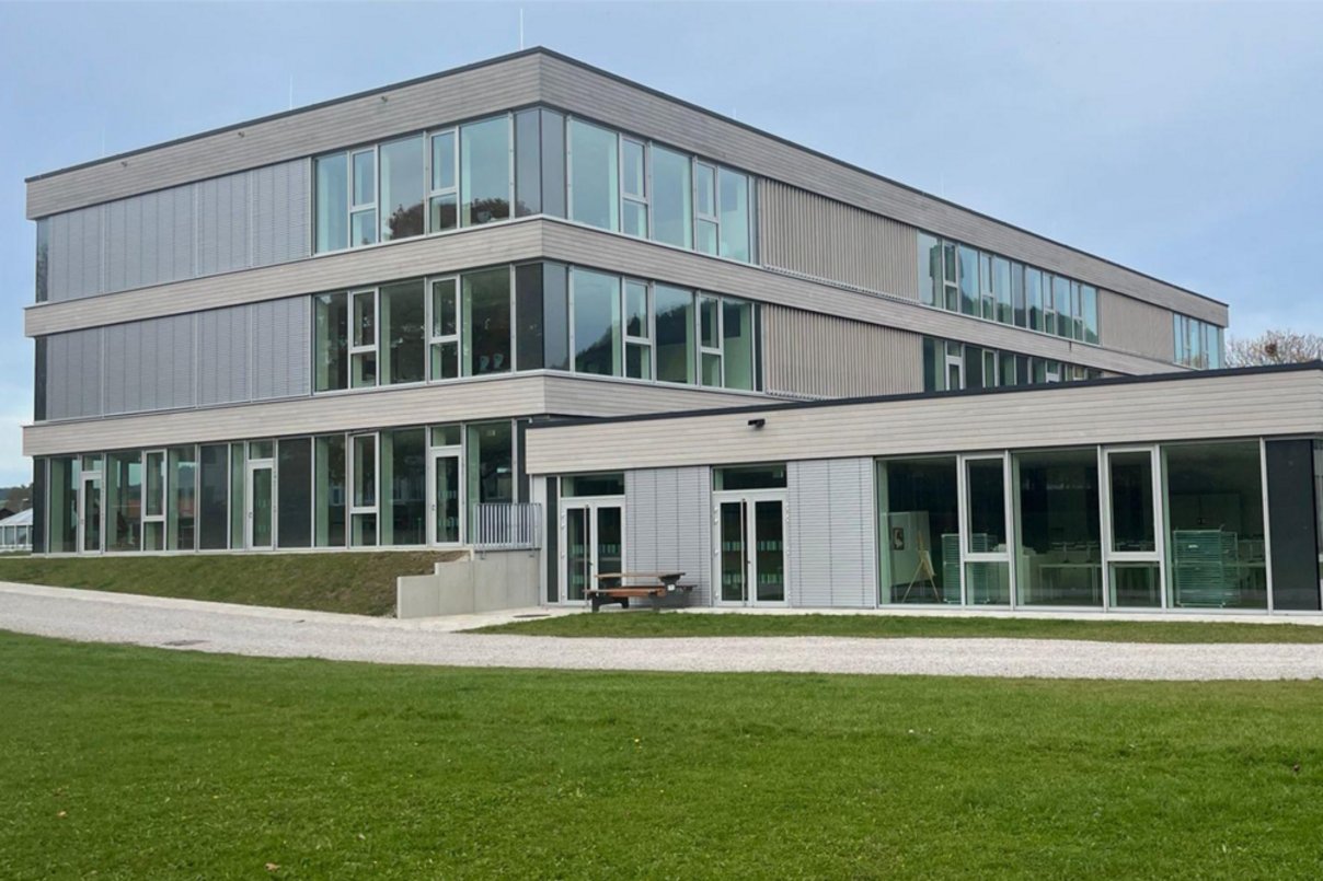 Modernes Schulgebäude dreigeschossig, davor Rasenfläche