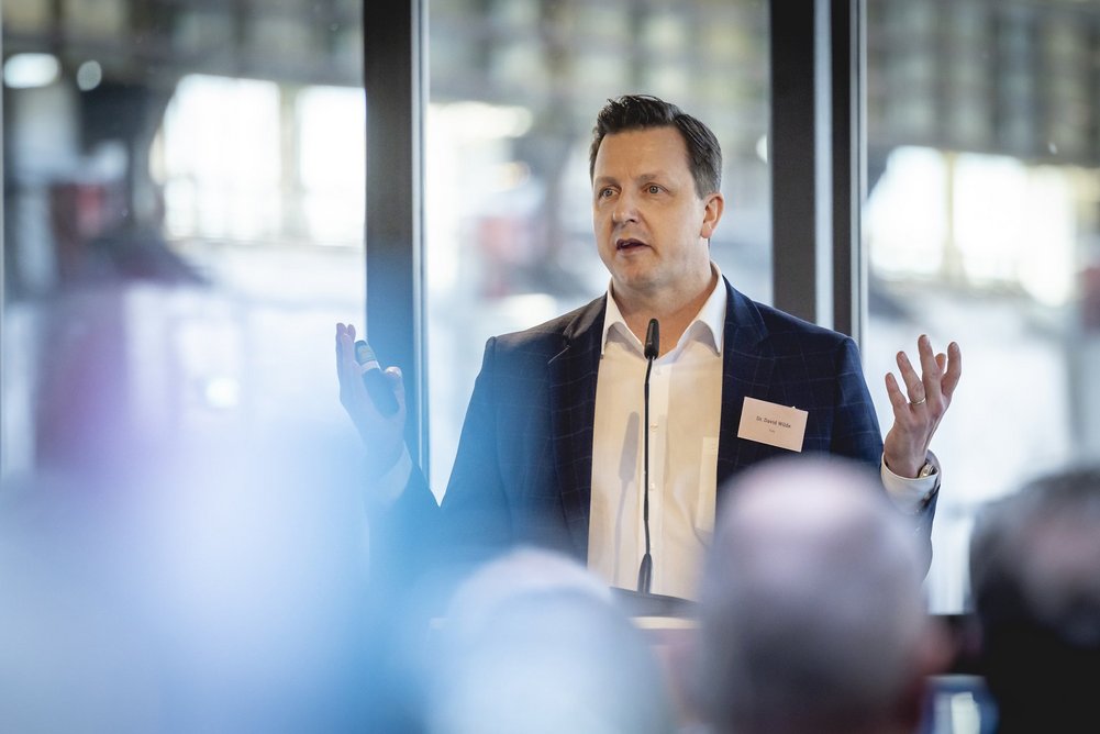 Dr. David Wilde Person in Business-Kleidung redet mit Handgestik vor Publikum.