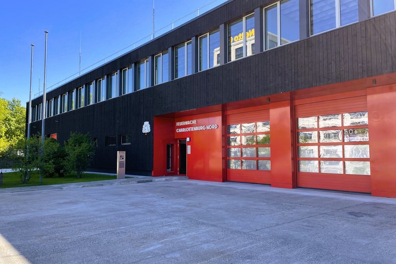 Außenansicht Feuerwache Charlottenburg nach Sanierung, Gebäude zweigeschossig, dunkle Holzfassade mit Fenstern, rote Torzufahrt