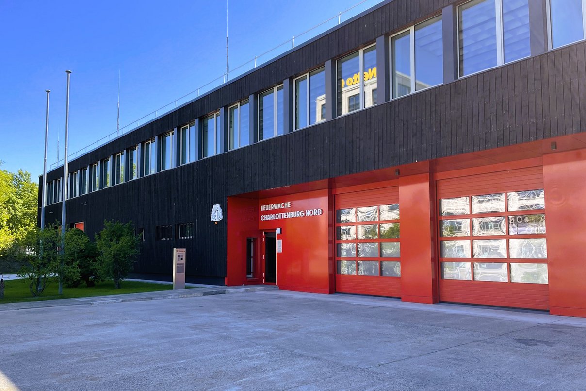Außenansicht Feuerwache Charlottenburg nach Sanierung, Gebäude zweigeschossig, dunkle Holzfassade mit Fenstern, rote Torzufahrt