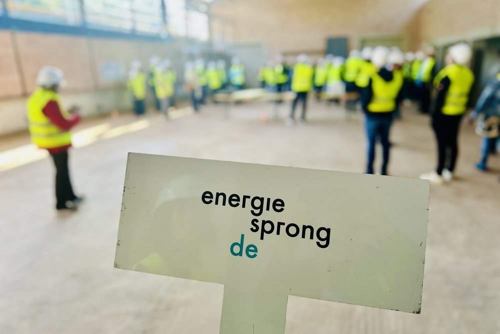 Bild zeigt im Vordergrund ein Schild mit Aufschrift Energiesprong und im Hintergrund eine Turnhalle