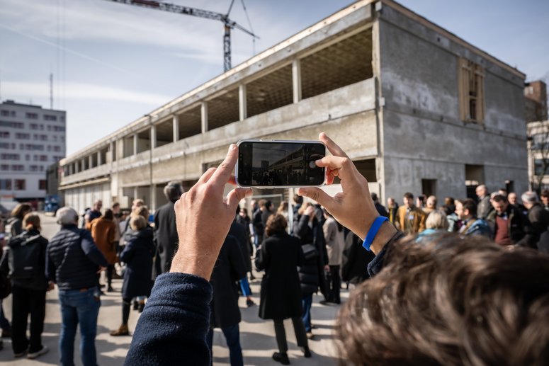 Gebäude im Rohbau, im Vordergrund Personengruppe
