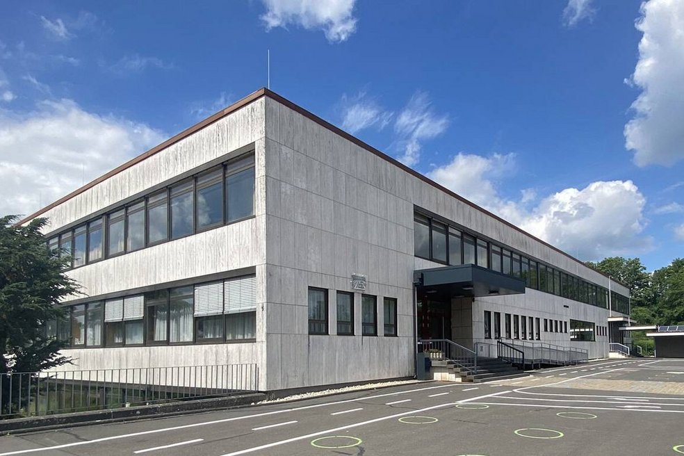 Unsaniertes Schulgebäude und Schulhof, blauer Himmel mit dicken weißen Wolken