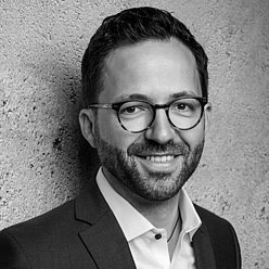 Kian Giahi Portraitfoto in Schwarz-Weiß, Person mit kurzen dunklen Haaren, Bart und Brille