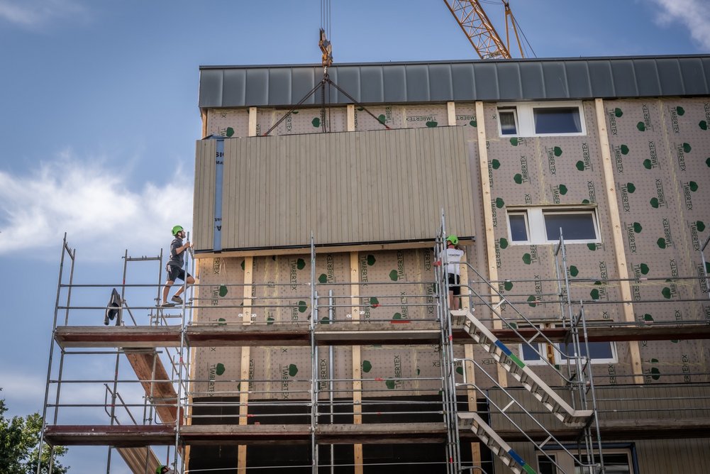 Vorgefertigtes Fassadenelement wird durch Bauarbeiter für die Montage am Mehrfamilienhaus platziert.