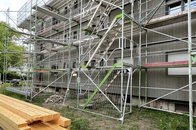 Mehrfamilienhaus mit Baugerüst, davor Rasenfläche mit liegenden Holzbalken