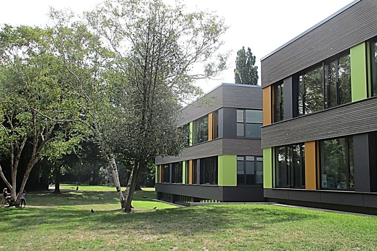 Saniertes Schulgebäude zweigeschossig mit Flachdach, davor Rasen und Bäume