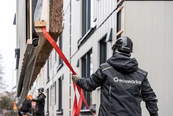 Bauarbeiter navigiert vorgefertigtes Hausfassadenelement per Seil.