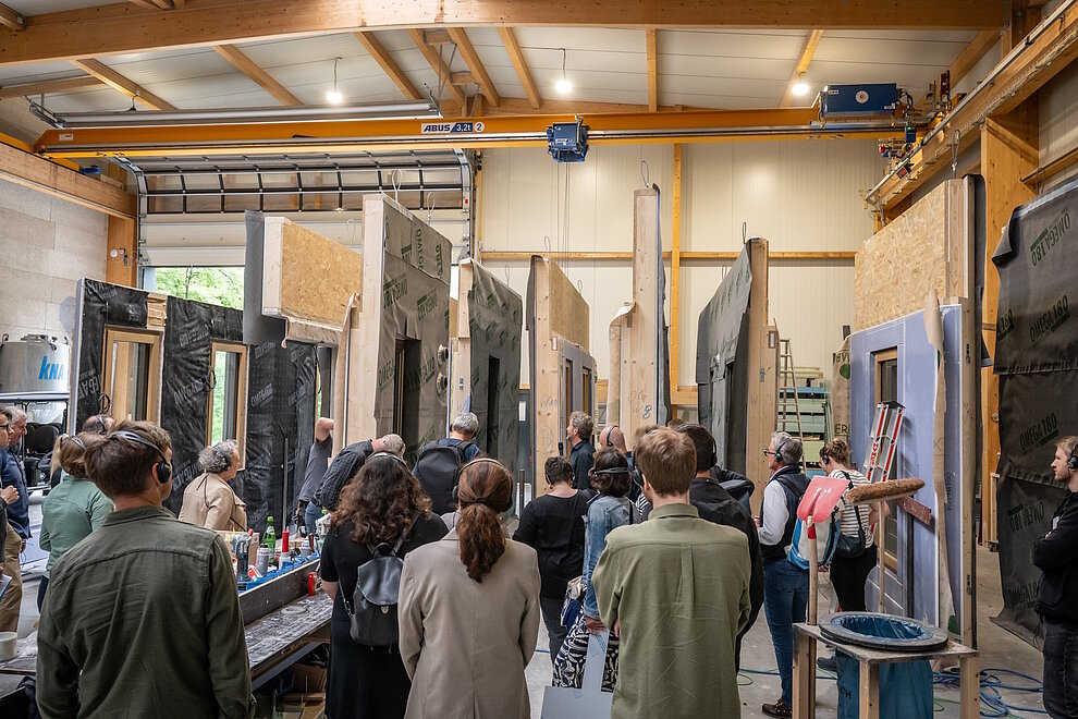 Werk von Holzbau Kappler, Fertigungshalle Personen schauen Vorfertigung von Hausfassadenelementen im Werk an.