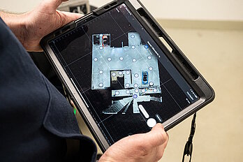 Tablet, das von zwei Händen gehalten wird. Auf dem Bildschirm eine digitale Gebäudeabbildung.