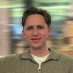 Person mit kurzen Haaren, sitzend, grüner Pullover