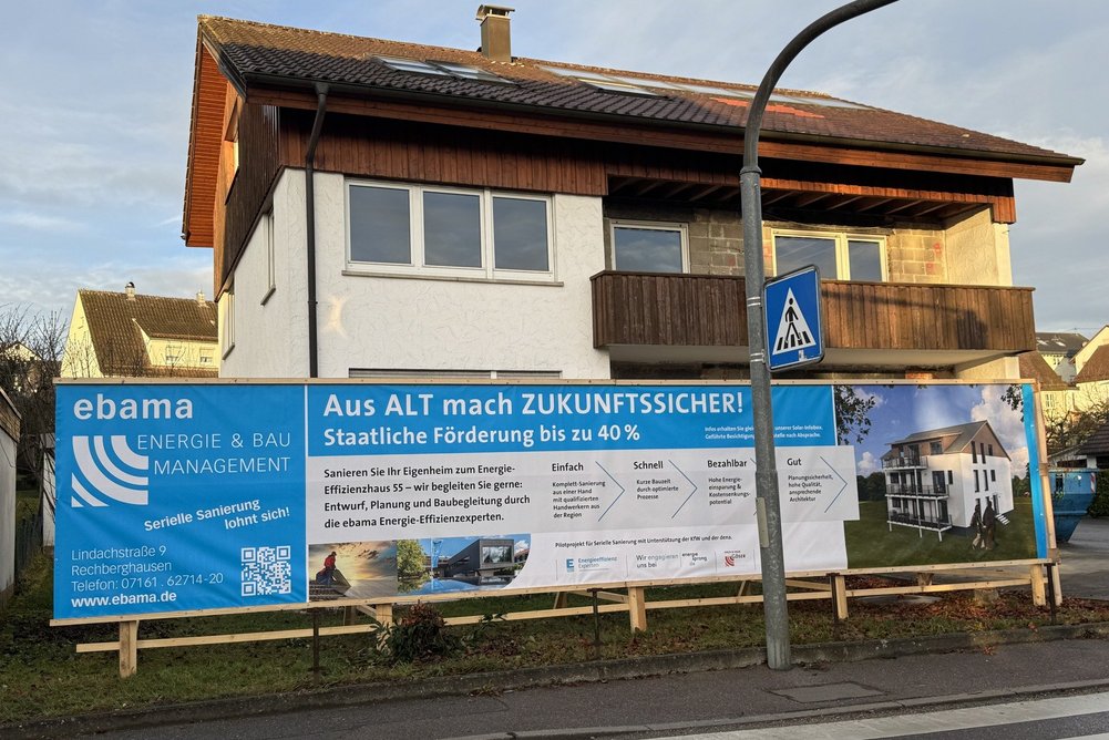 Bild zeigt: Straßenansicht eines Hauses mit Bauschild davor