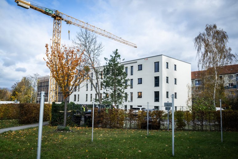 Viergeschossiges Gebäude mit Flachdach während der Sanierung, davor ein Kran und drumherum Grünflächen.