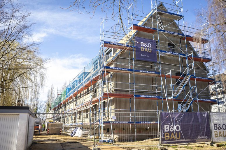 Seitlicher Blick auf ein Mehrfamilienhaus zweigeschossig mit Schrägdach während Sanierung, Baugerüst, im Hintergrund leicht bewölkter blauer Himmel