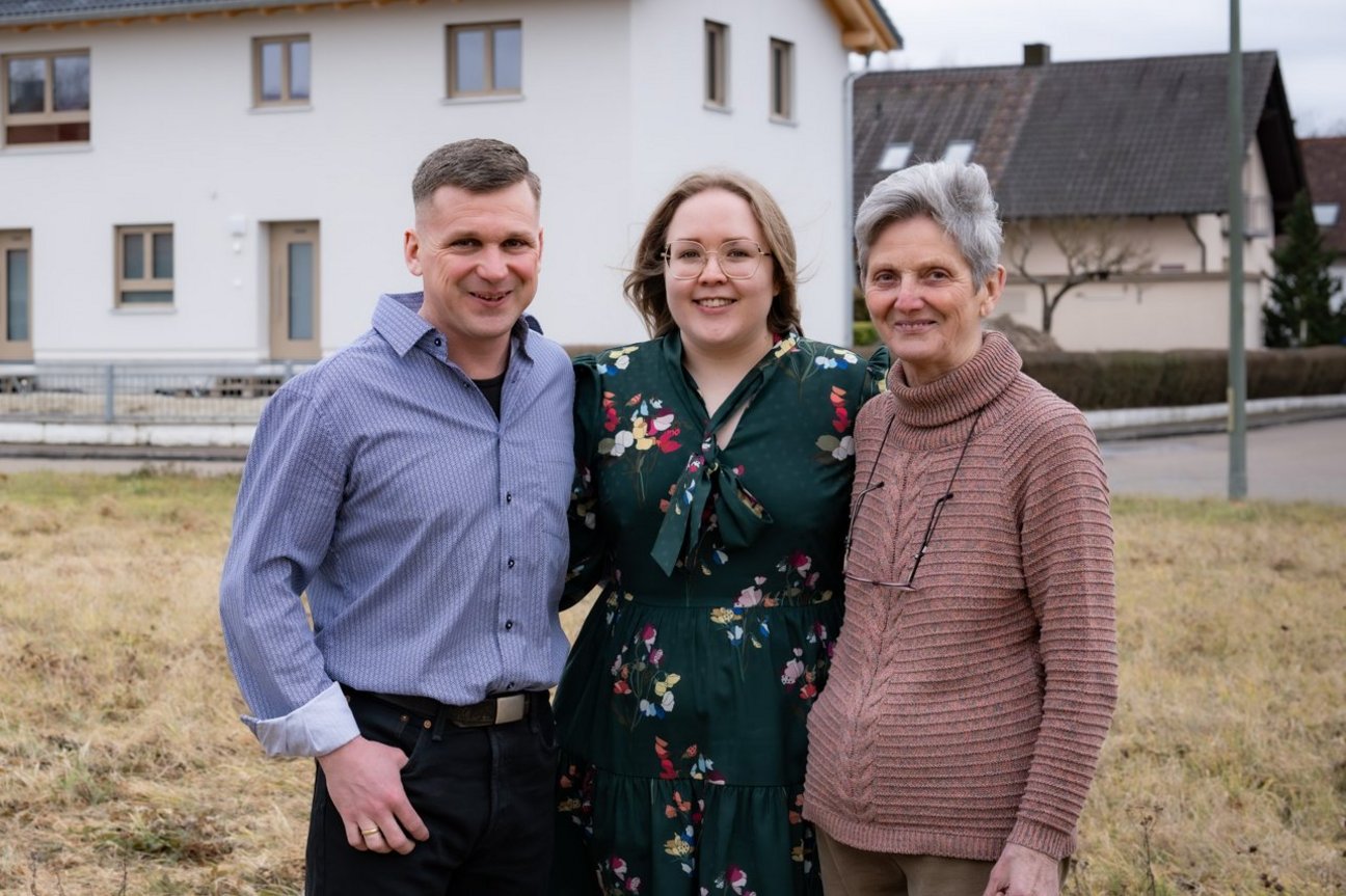 Zwei Generationen unter einem Dach. Drei Menschen vor einem neu sanierten Haus, die sich umarmen