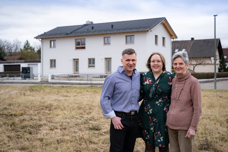 Drei Menschen vor einem neu sanierten Haus, die sich umarmen