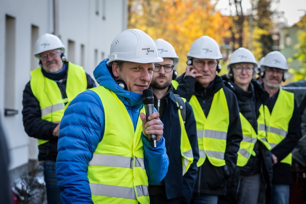 Personen hören einem Vortragenden zu, der in ein Handmikrofon spricht.