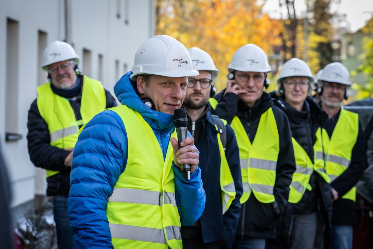 Personen hören einem Vortragenden zu, der in ein Handmikrofon spricht.