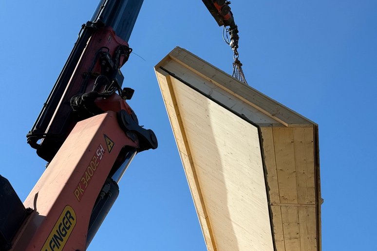Bild zeigt Kranarm mit Holzelement daran hängend