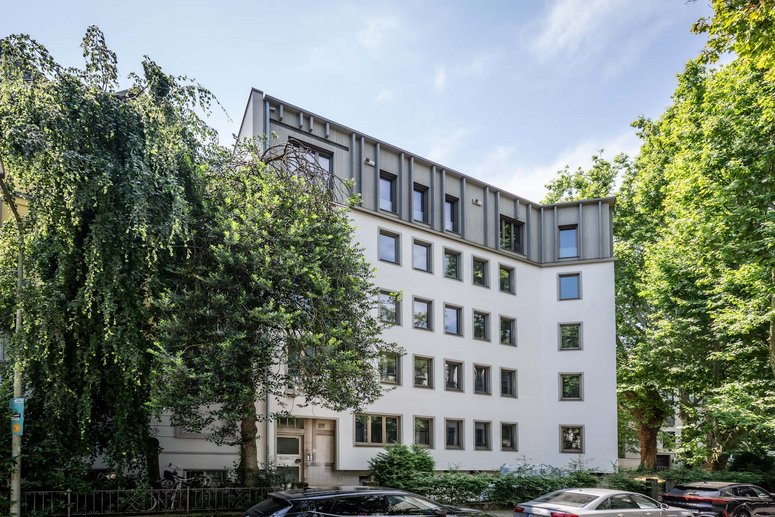 Mehrfamilienhaus neu saniert, Laubbäume links und rechts davon, davor eine Straße